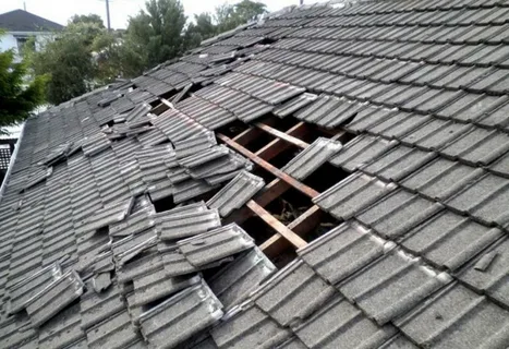 Storm-damaged tiled roof with exposed rafters and displaced tiles, showing why hail damage roof repair is urgent